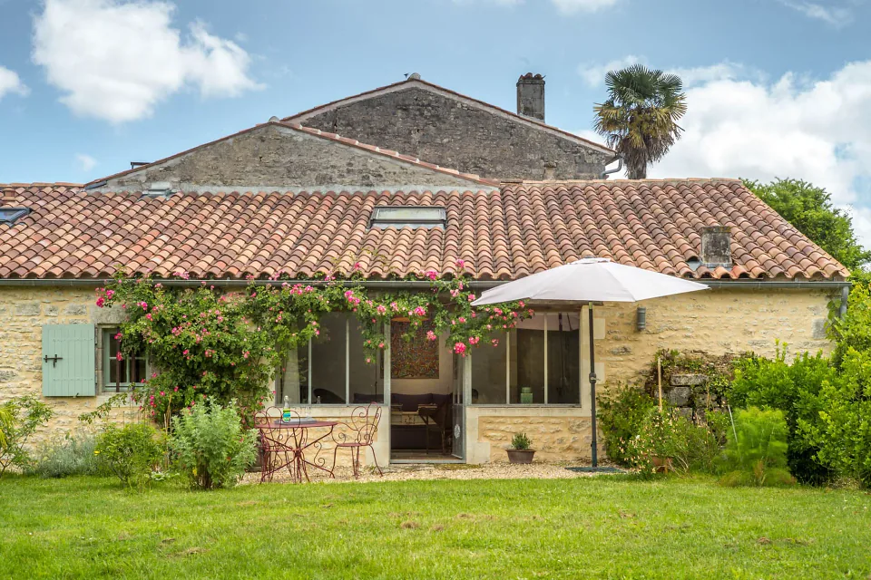 Le gîte vu de la pelouse, parasol ouvert devant la terrasse fleurie