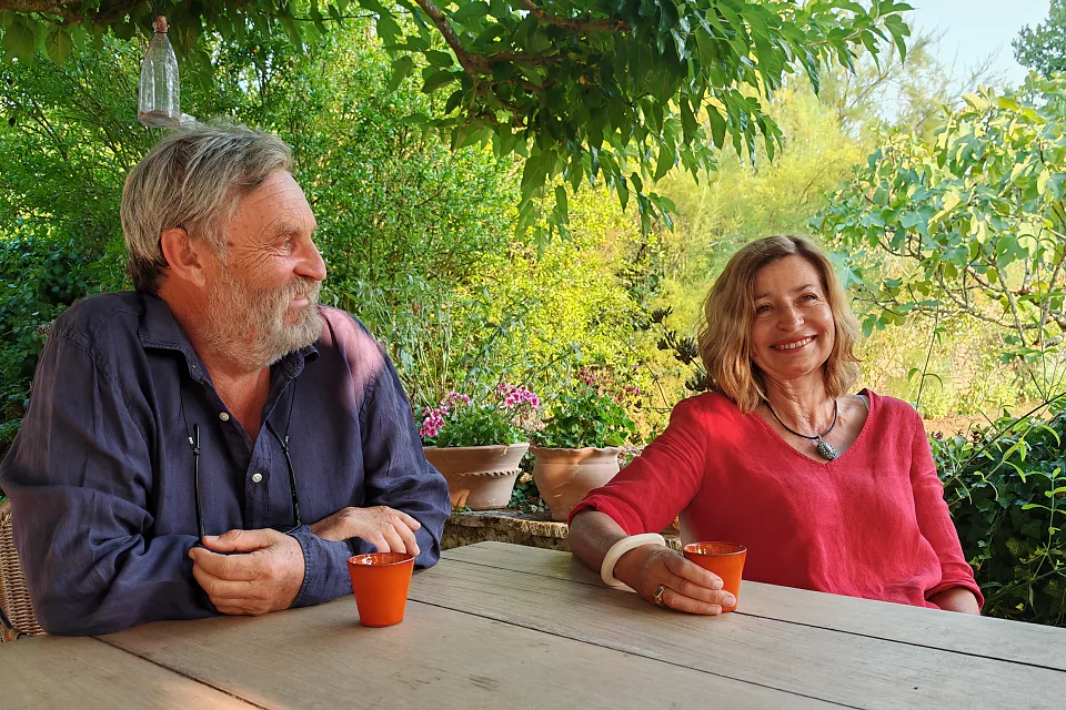 Laurence et Pierric attablés au jardin, sous le feuillage, un verre à la main