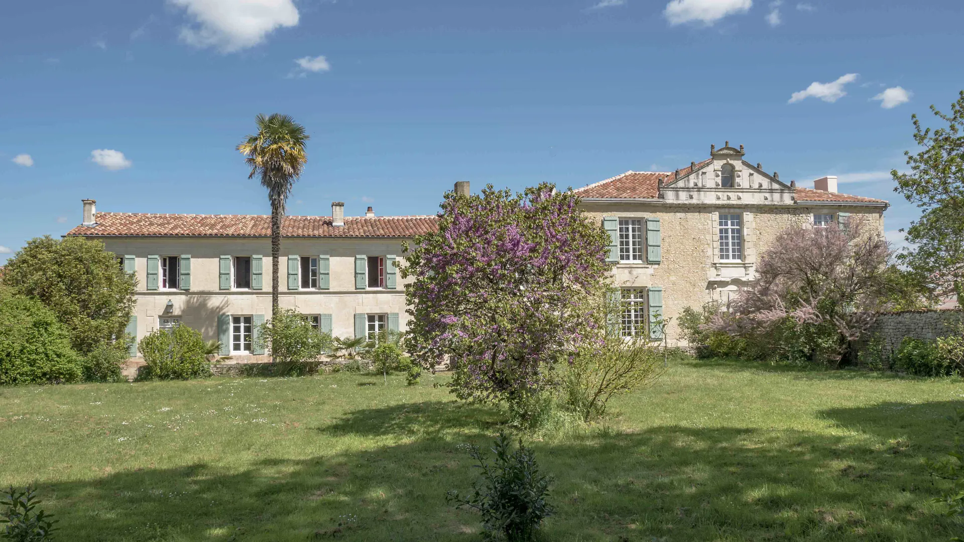 La façade du Logis de l'Épinière au printemps, palmier et arbre de Judée en fleurs