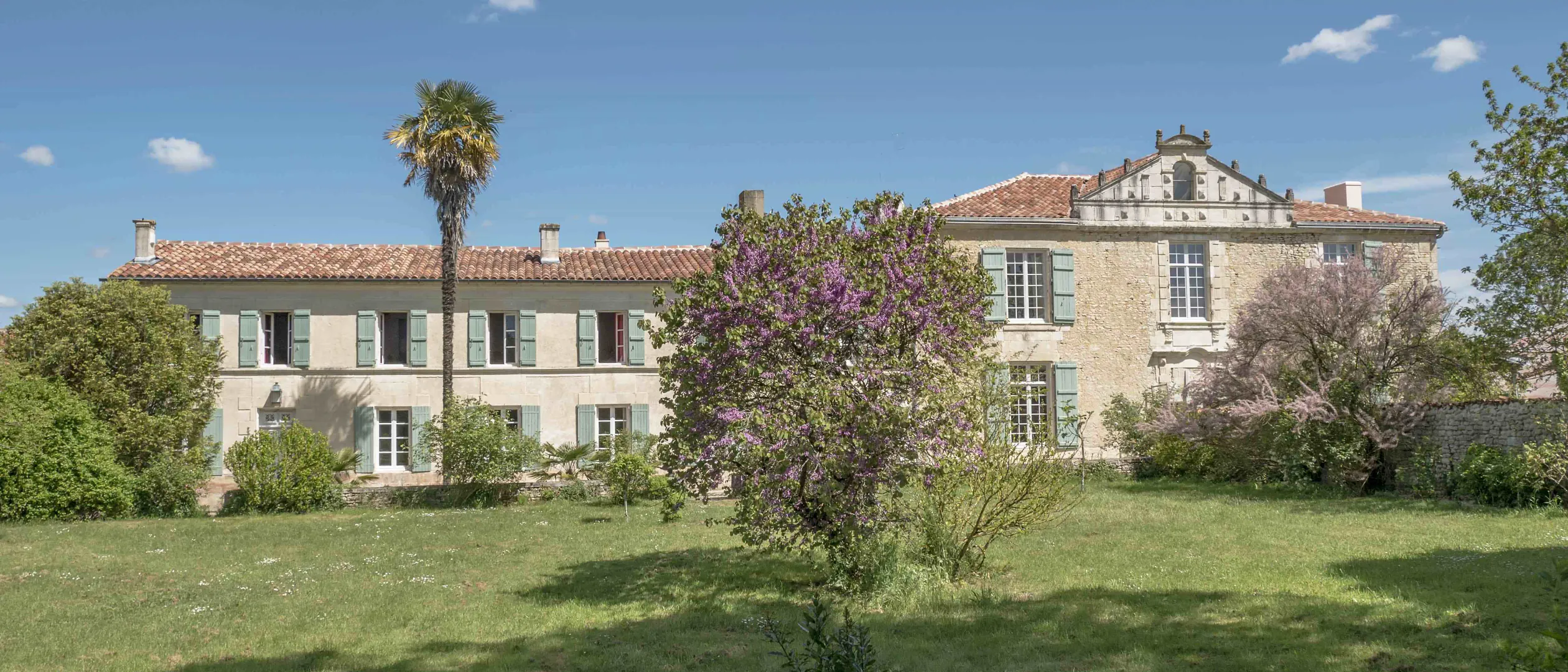 La façade du Logis de l'Épinière au printemps, palmier et arbre de Judée en fleurs