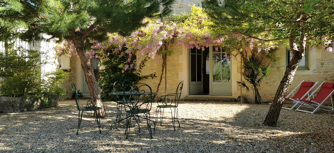 Terrasse de gravier de Bons Bois sous la glycine, table et chaises en fer, transats à l'ombre