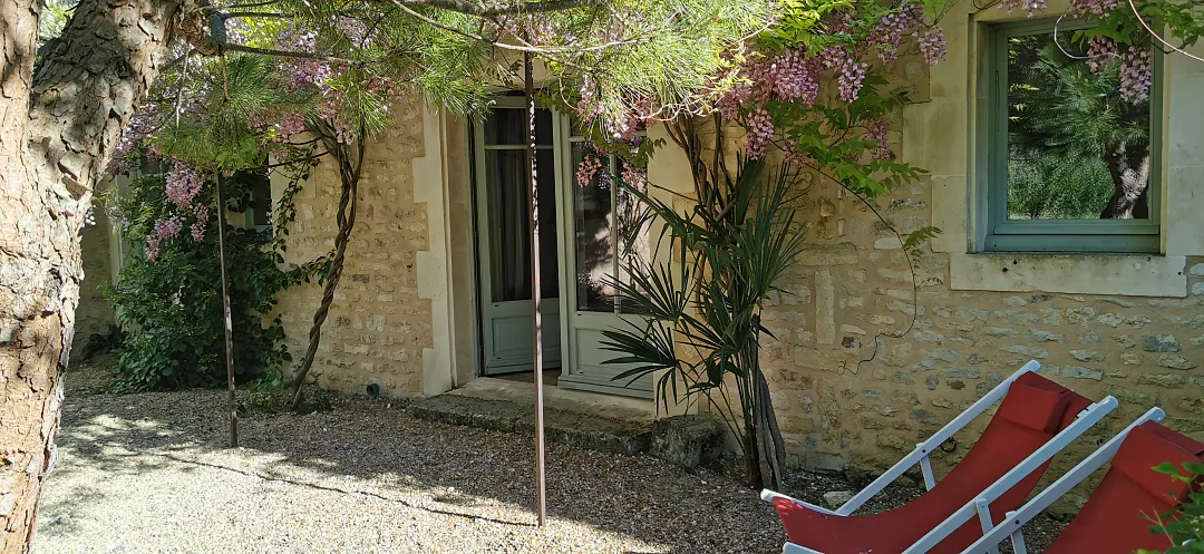 Terrasse de Bons Bois sous la glycine en fleurs, transats devant la façade de pierre