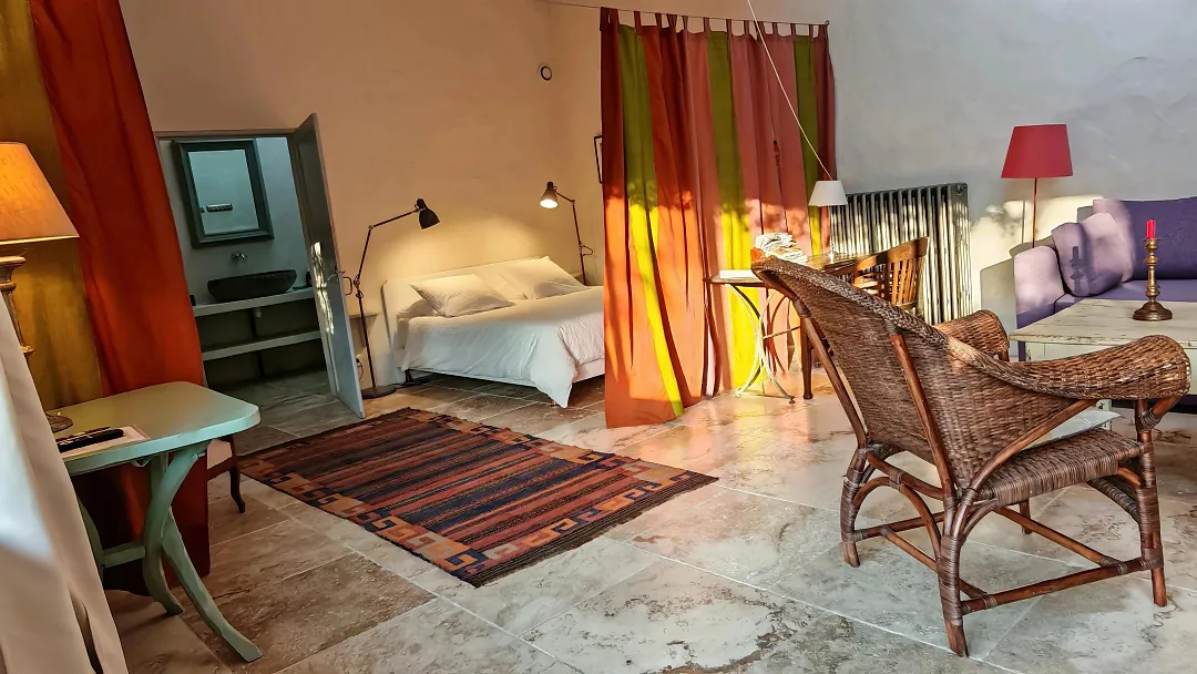 Chambre de Borderies vue depuis le séjour, rideaux orange et vert, tapis kilim et fauteuil en rotin