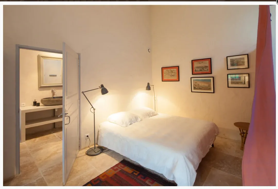 Chambre de Borderies, lit double blanc, série de gravures encadrées et porte ouverte sur la salle d'eau