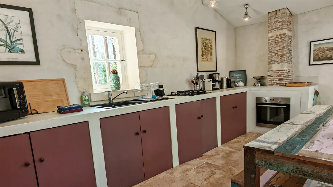 Cuisine de Borderies avec four encastré et mur de pierre apparente, fenêtre à petits carreaux