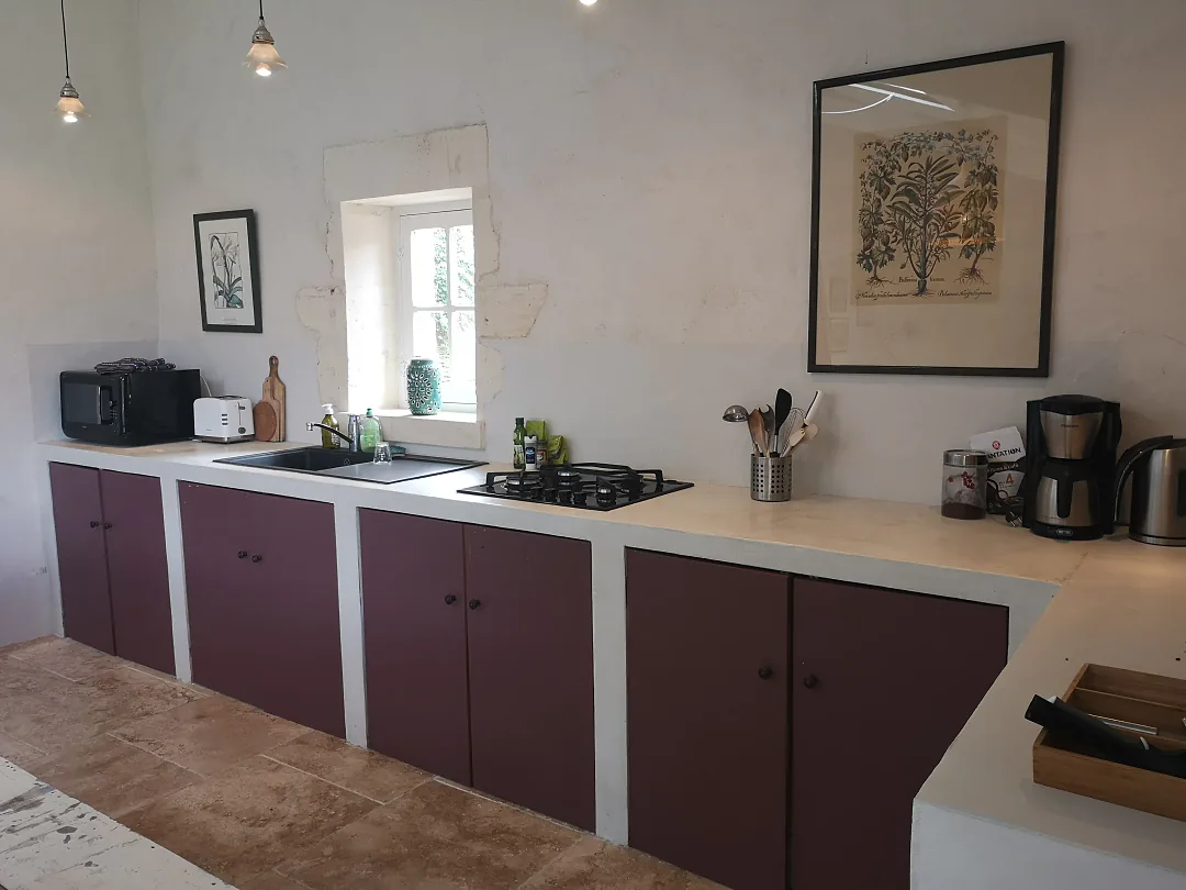 Cuisine ouverte du gîte Borderies, façades aubergine et plan de travail blanc, évier sous la fenêtre