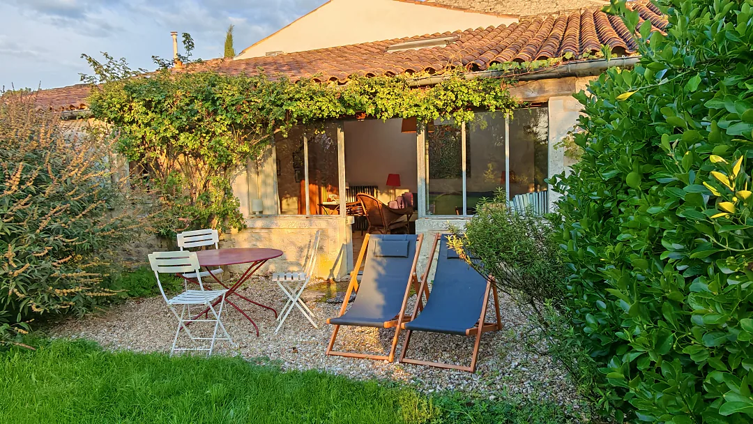 Terrasse de Borderies abritée sous la treille, salon de jardin et transats bleus sur la pelouse