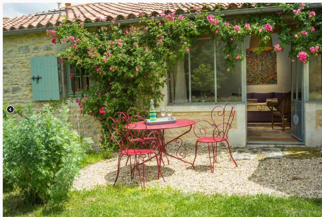 Terrasse de gravier de Borderies, guéridon et chaises en fer rouge sous le rosier grimpant