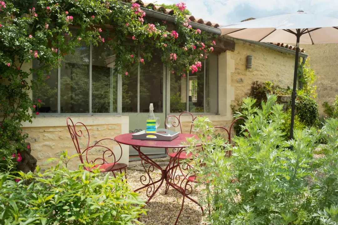 Terrasse de Borderies vue de face, parasol et rosier en fleurs le long des baies vitrées