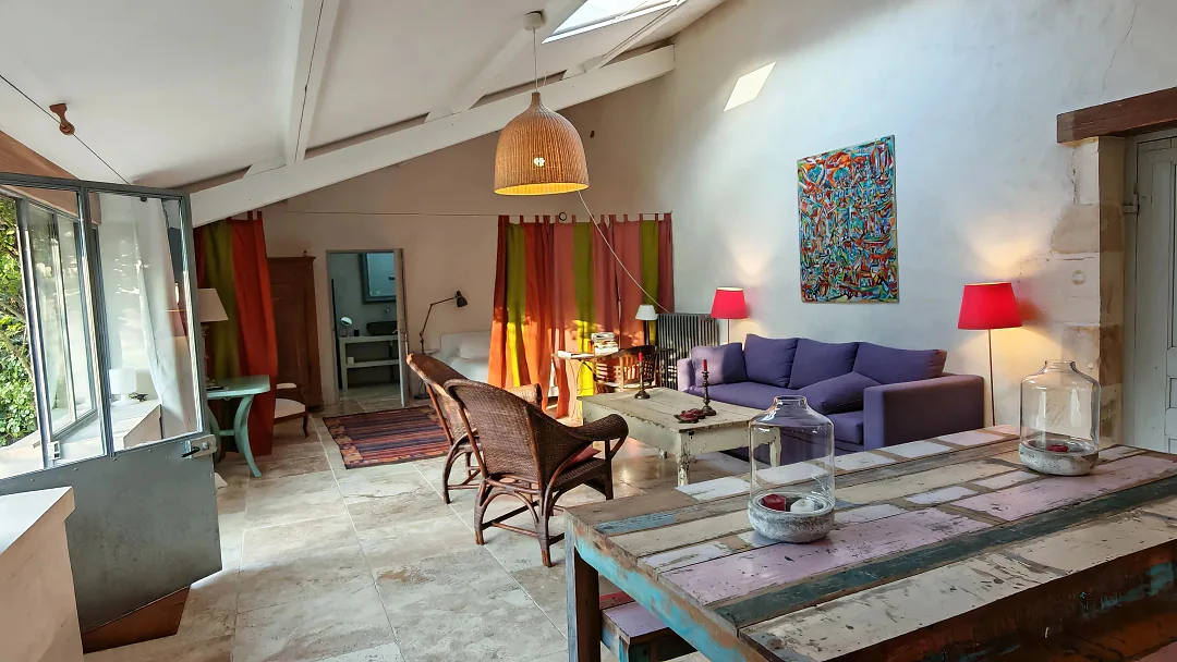 Séjour du gîte Borderies sous charpente blanche, canapé violet et fauteuils en rotin, baies ouvertes sur le jardin