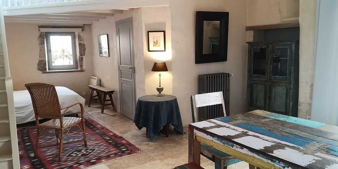 Chambre de Fins Bois, fauteuil en rotin et guéridon près de la fenêtre à linteau de pierre
