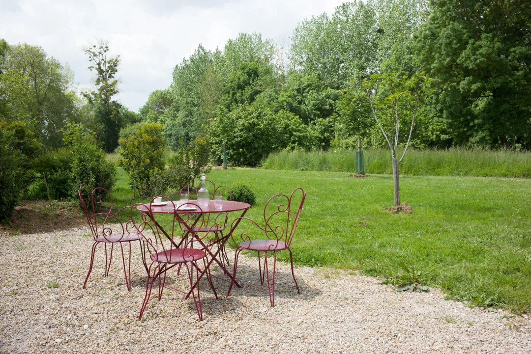 Guéridon et deux chaises en fer sur la terrasse de gravier de Fins Bois, prairie arborée