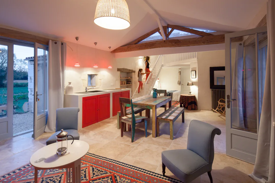 Séjour du gîte Fins Bois sous charpente apparente, table en bois, fauteuils gris et porte-fenêtre