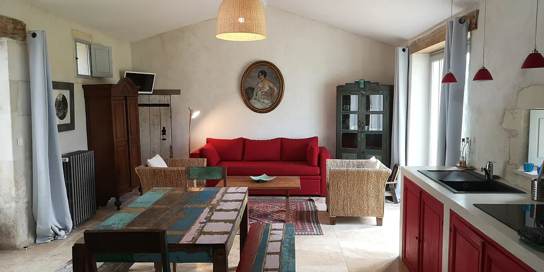 Vue d'ensemble du séjour de Fins Bois, canapé rouge et tapis kilim, cuisine ouverte au fond