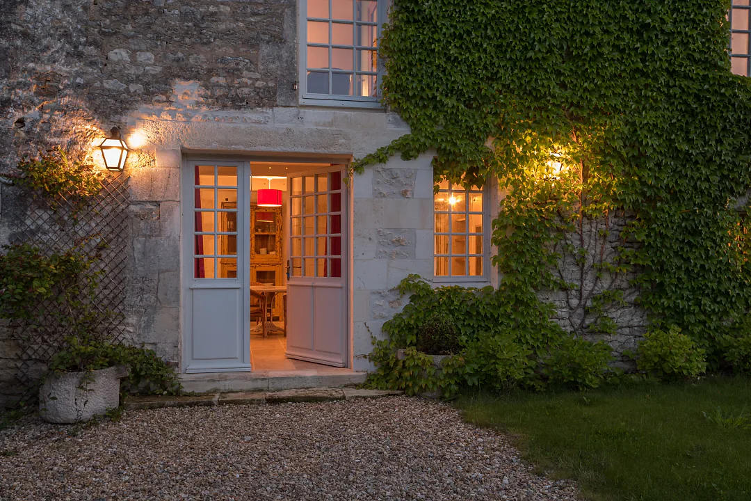 La façade de pierre couverte de lierre du gîte Grande Champagne, fenêtres éclairées au crépuscule
