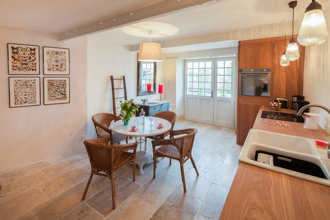 Coin repas de Grande Champagne, table ronde et chaises en rotin devant la cuisine en bois