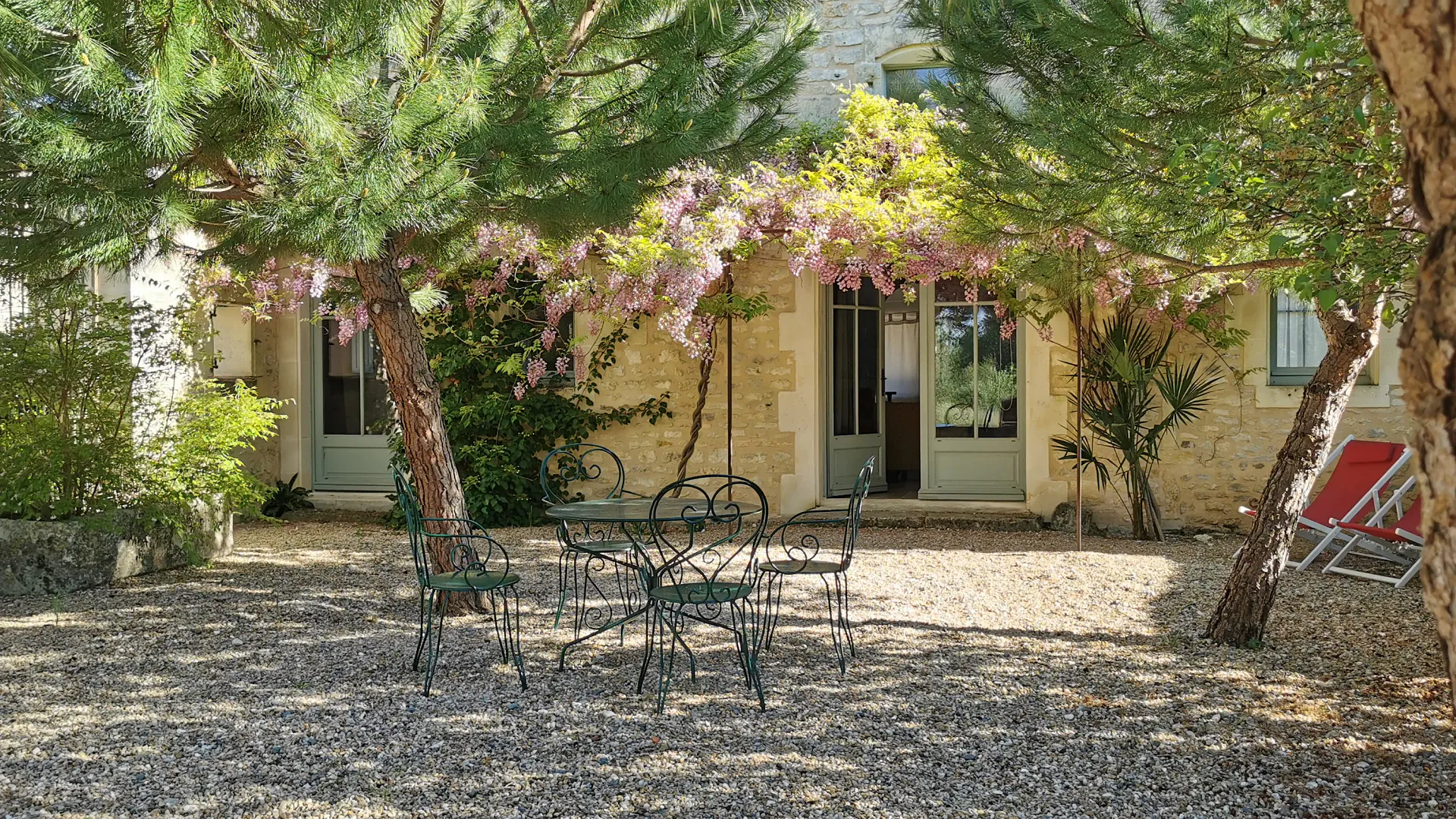 La cour du Logis sous la glycine, table et chaises devant la maison ouverte